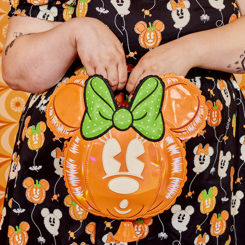 Woman holding the Minnie Mouse Pumpkin Balloon Crossbody Bag to camera, which has Minnie Mouse as a "mylar foil" balloon looking to her left. 